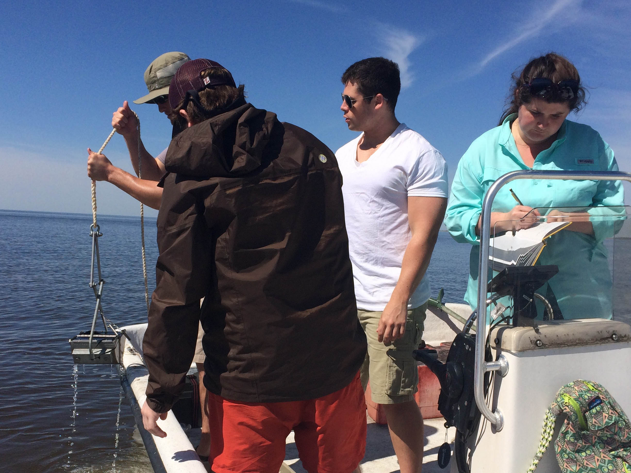 Students collect seafloor sediment samples in the Mississippi Sound and record sampling notes