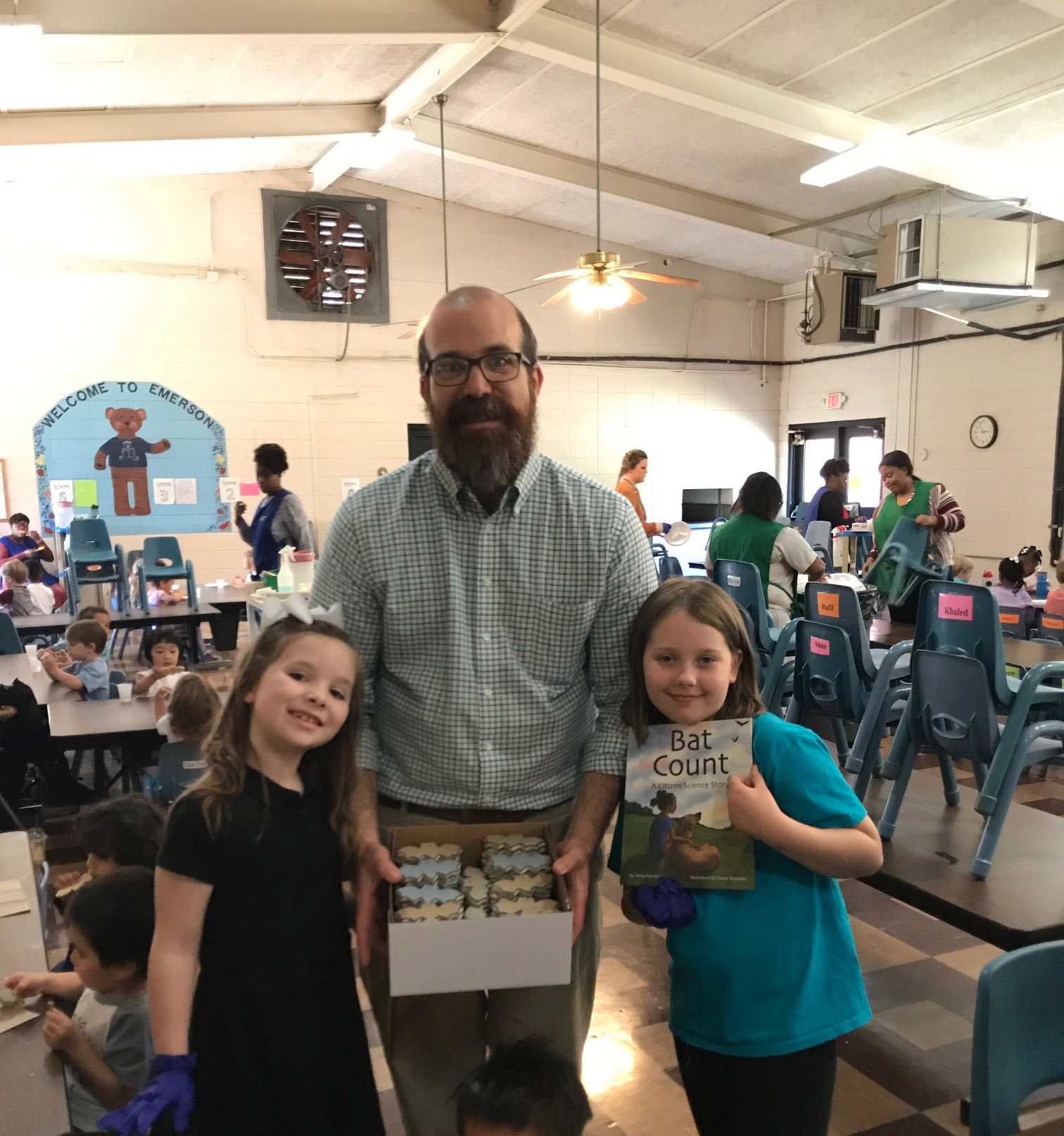 Dr. Ryan Walker, MSU Department of Curriculum, Instruction, and Special Education, is assisted by Mary Mack Walker (left) and Margot Hoffman (right) in handing out bat cookies to Emerson Family School students, in celebration of the 2018 Giverny Award.