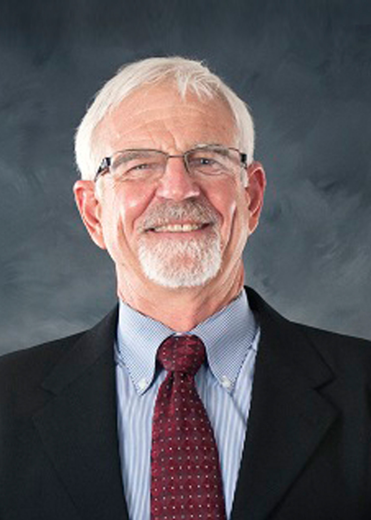 Professional photo of Bill Cooke, wearing a black suit and red tie against a gray background.