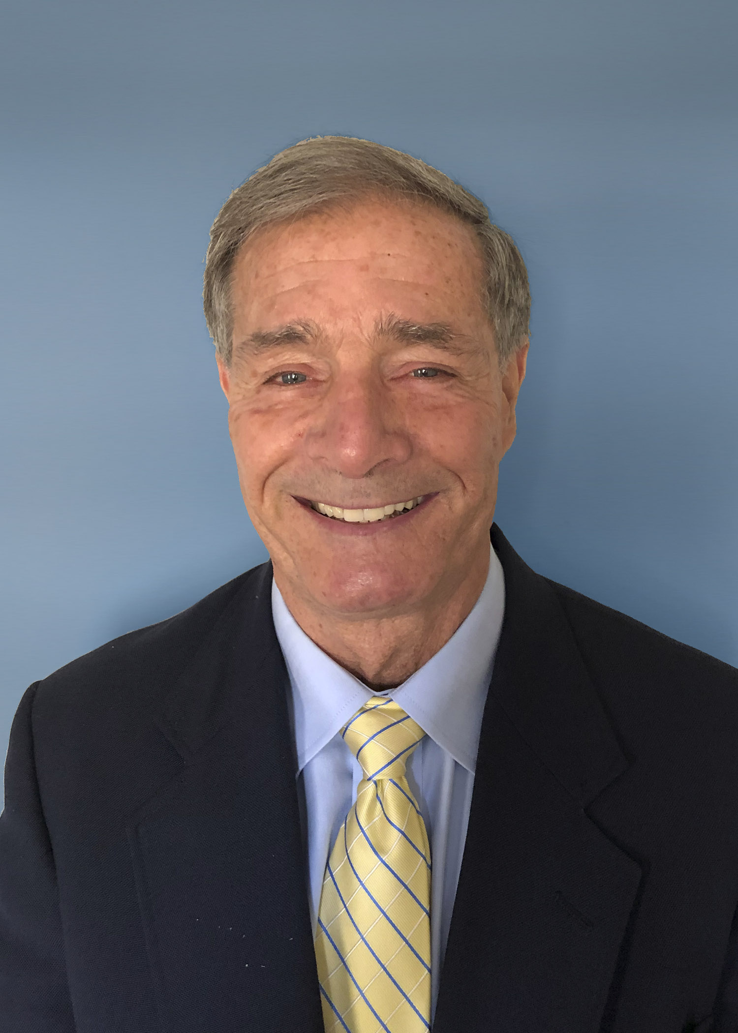Photo of Charles Wax wearing a dark suit on a blue background. 