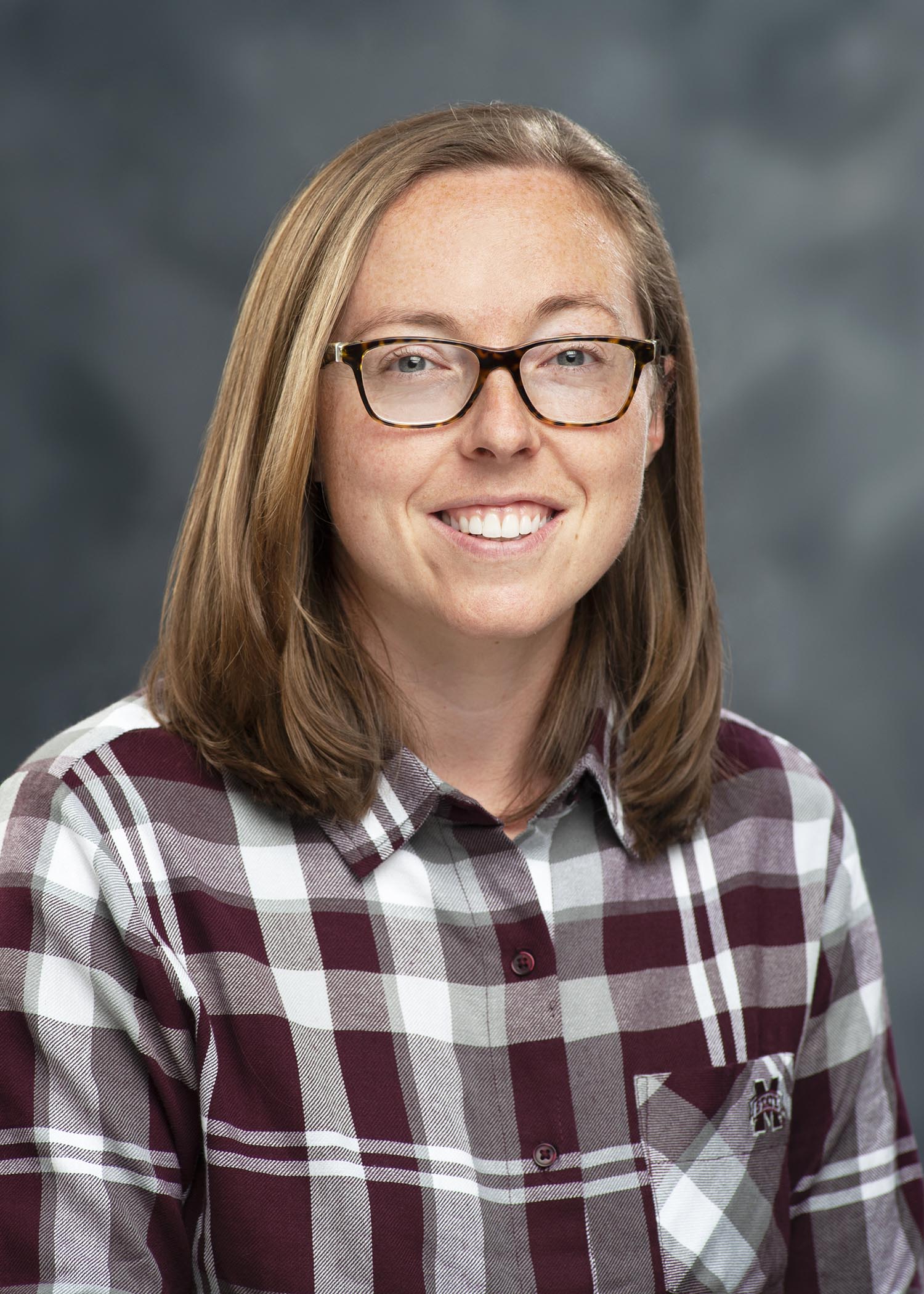 Professional photo of Kelsey Crane, wearing a maroon/white shirt against a gray background.