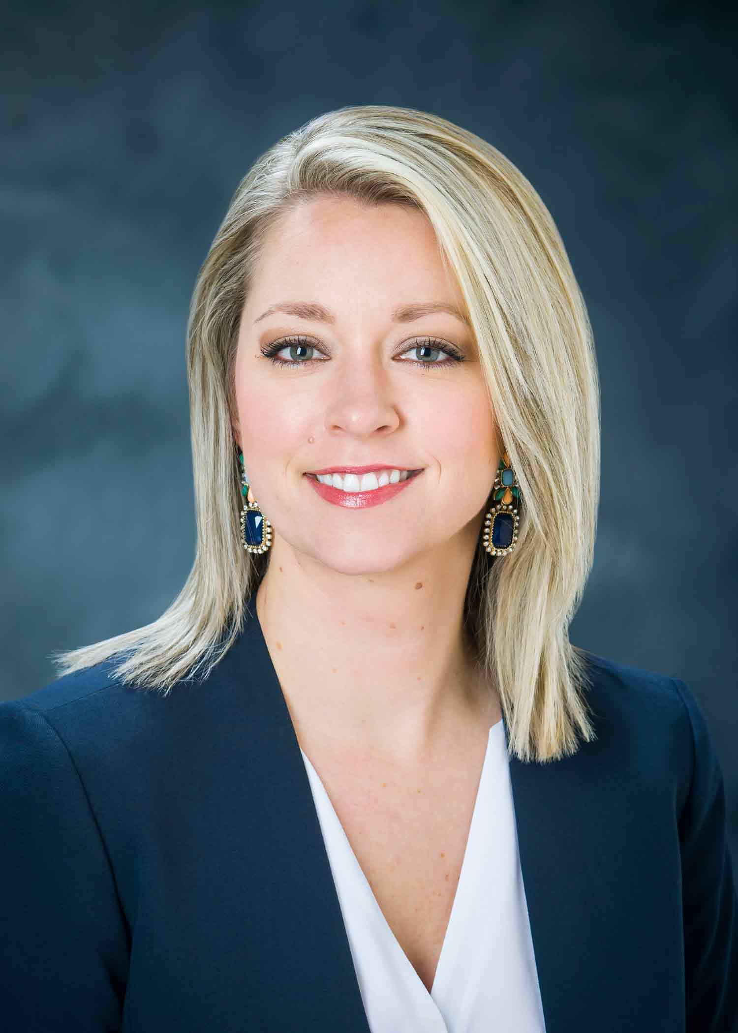 Professional photo of Lindsey Poe, wearing a white blouse and dark blazer against a blue background.