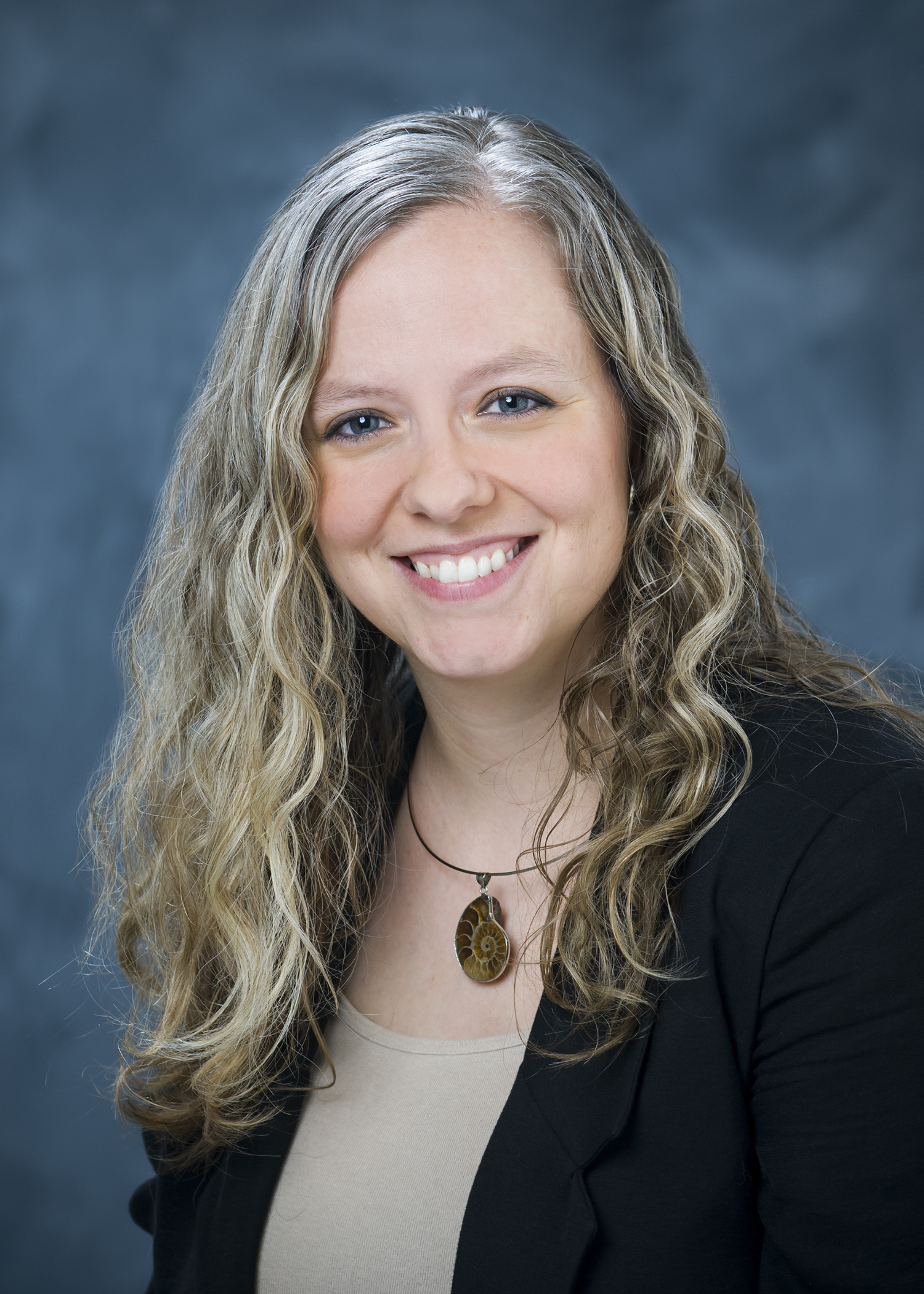 Professional photo of Athena Owen Nagel, wearing a beige shirt and dark blazer against a blue background.
