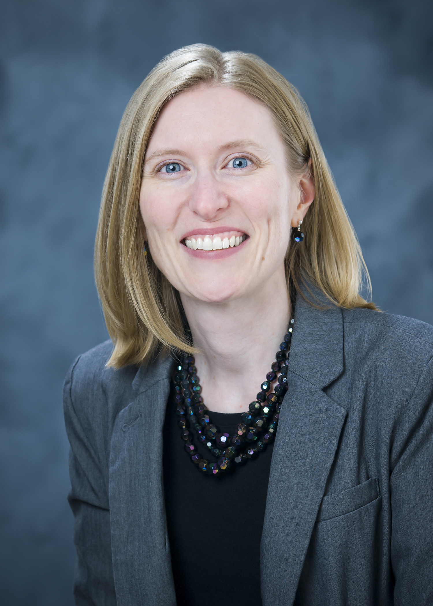 Professional photo of Kathy Sherman-Morris, wearing a black shirt and gray blazer against a blue background.
