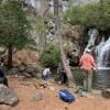 Five students take pictures and sketch while discussing whether or not to cross water to get to more rock outcrop