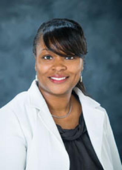 Professional photo of Yasma Jacobs, wearing a black blouse and white jacket against a blue background.